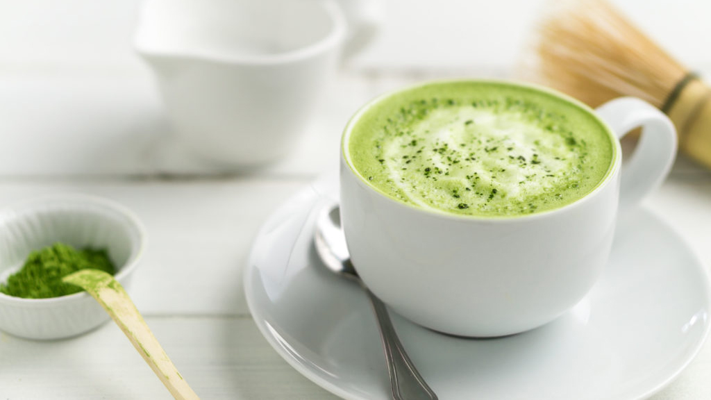 Tasse Matcha-Tee mit einem Löffel Matcha-Pulver daneben