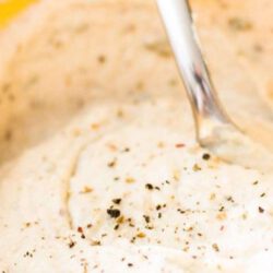 Der vegane Käse aus Cashewnüssen wird mit Kräutern verfeinert und in einem Behälter mit fröhlicher Farbe serviert.